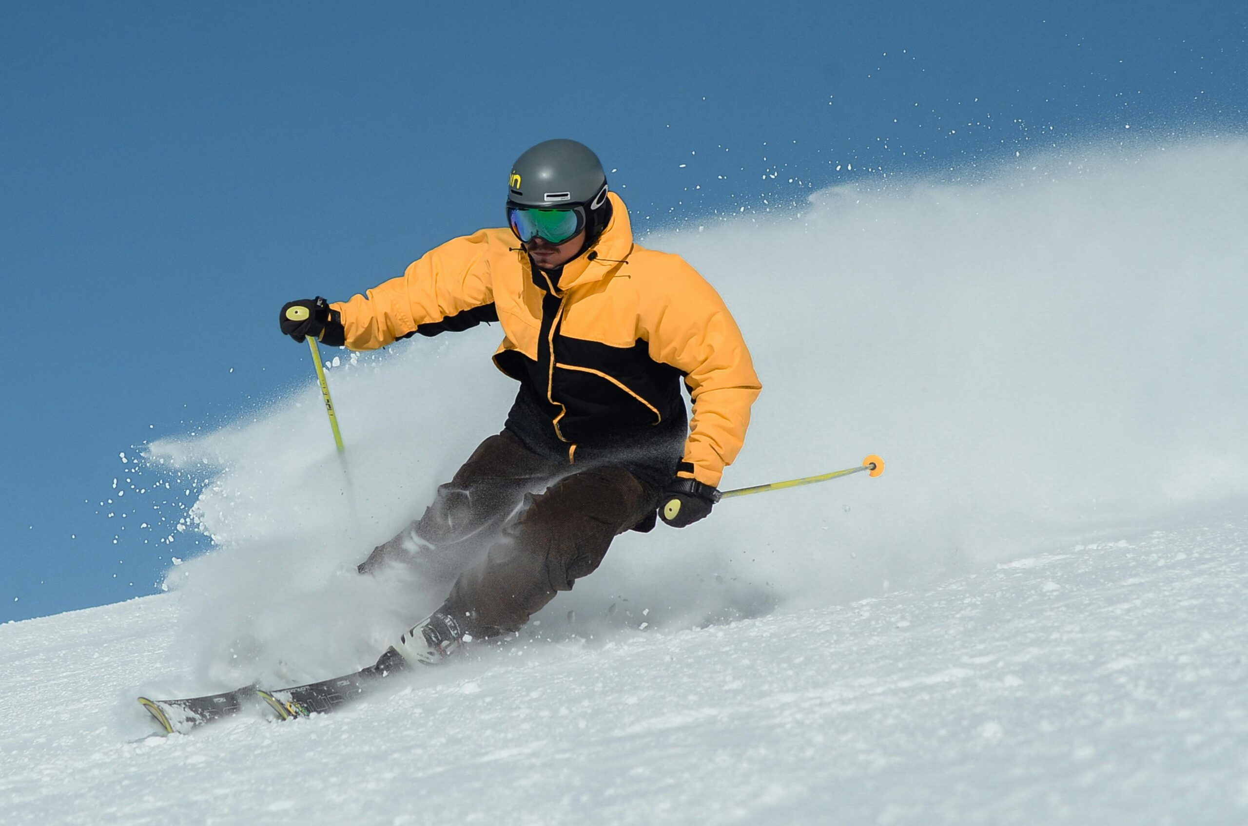 A focused skier wearing a bright jacket expertly navigating a snowy slope under clear skies.